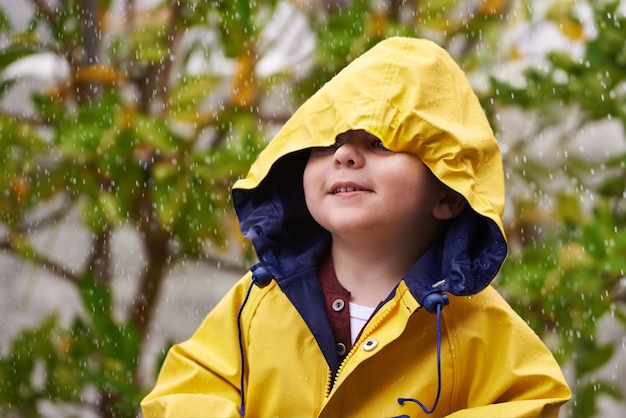 Photo child rain and raincoat outdoor in winter for fashion jacket and cold weather in london little boy male toddler and kid in drizzle by tree bokeh or environment with windbreaker for chilly season