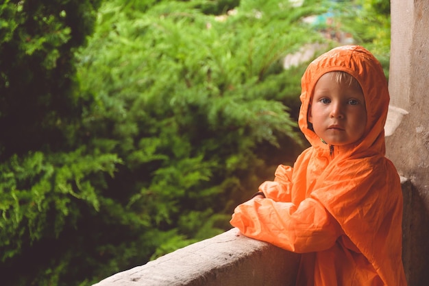 Child in a raincoat looks at the rain pensive child in an orange raincoat