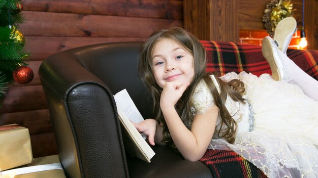 A child reads an interesting book by the Christmas tree.