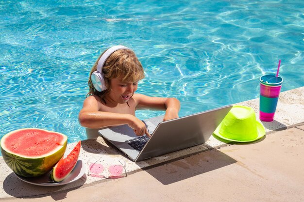 Child relaxing in the pool using laptop computer in summer water Kid boy online study or working on tropical sea beach Technology for life concept