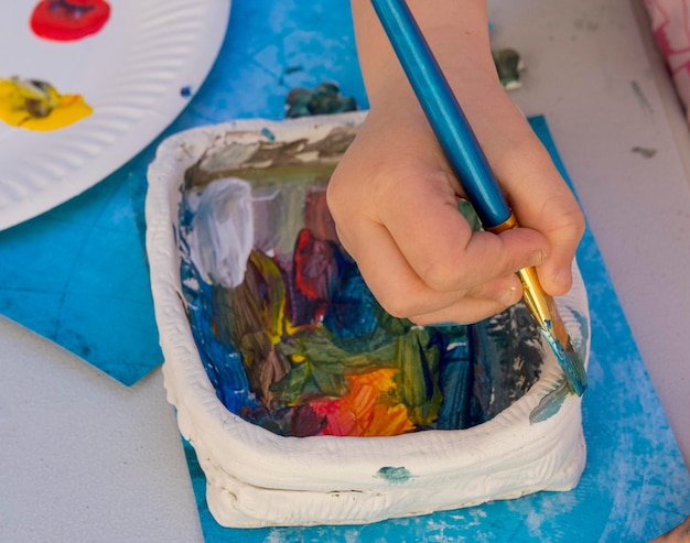 A child's hand holds a paintbrush and paints on a paper.