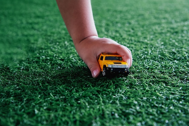 The child's hand holds a yellow toy car against the background of green grass