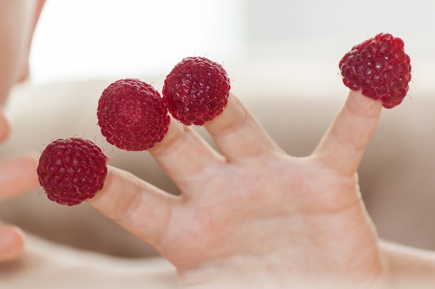 Child's hand with raspberries on fingers