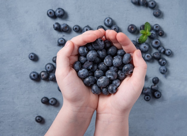 The child's hands hold a blueberries over the blue table