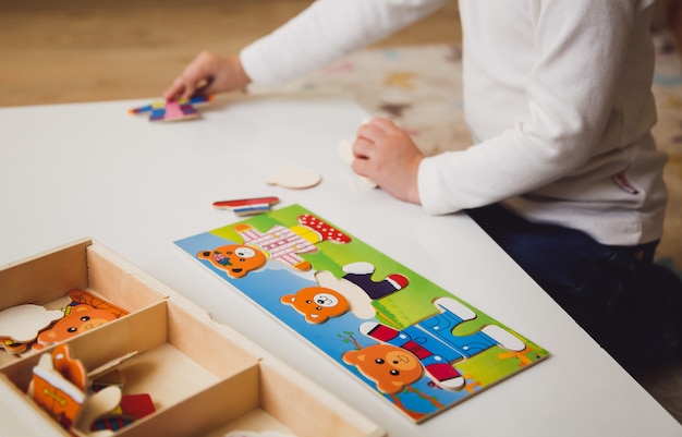 Child's hands with colorful board game on the white table.