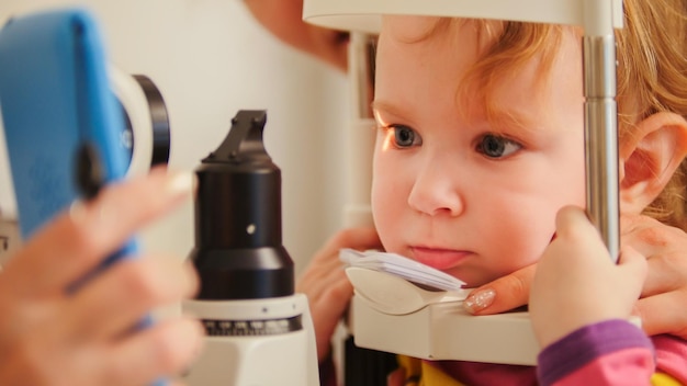 Child's optometry - little girl checks eyesight in eye ophthalmological clinic - close up, telephoto