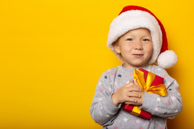 Child in a Santa Claus hat holds a gift