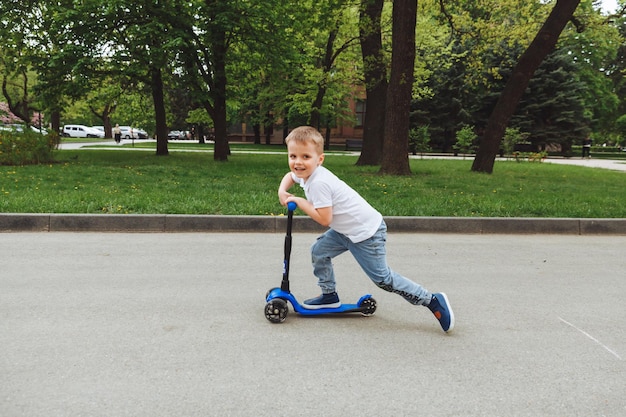 Photo child on a scooter in the park a little boy rides a scooter on a sunny day active sports for preschoolers