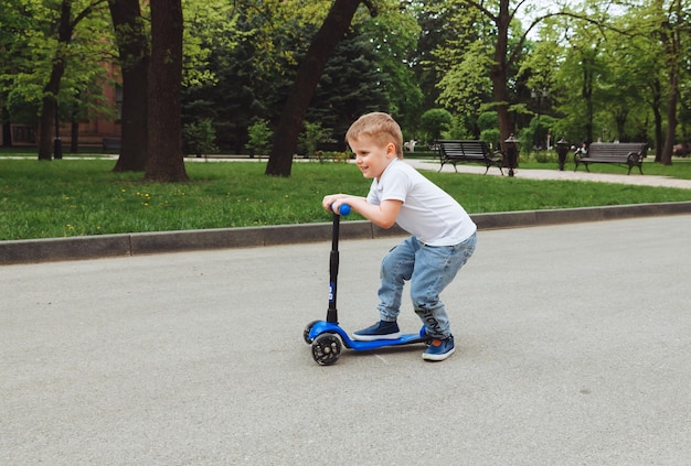 Photo child on a scooter in the park a little boy rides a scooter on a sunny day active sports for preschoolers