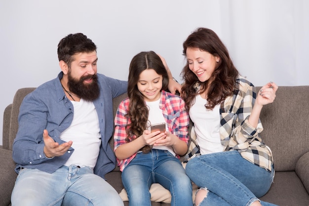 Child share news with mother and father Little girl child use mobile phone Happy family at home Buy online Child with childhood happiness bearded man and woman with child Family bonds