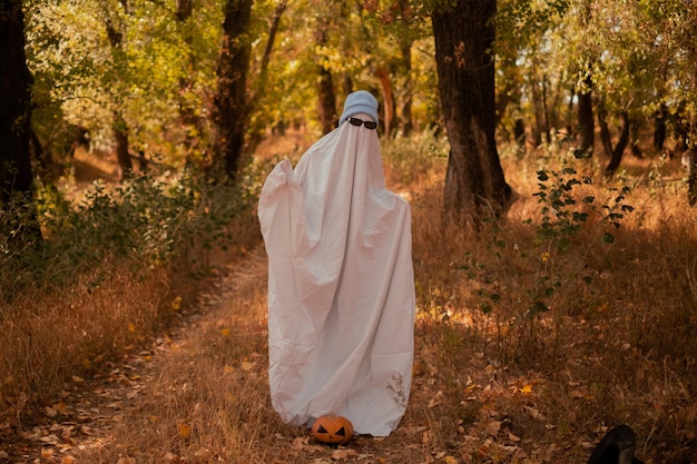 A child in sheets wearing black glasses looking like a ghost costume in the autumn forest