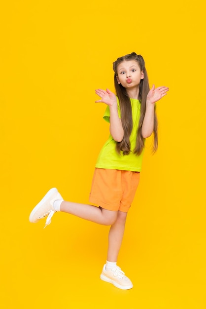 A child in shorts and a Tshirt Happy childhood A little girl with long hair enjoys the warmth in summer clothes on a yellow isolated background