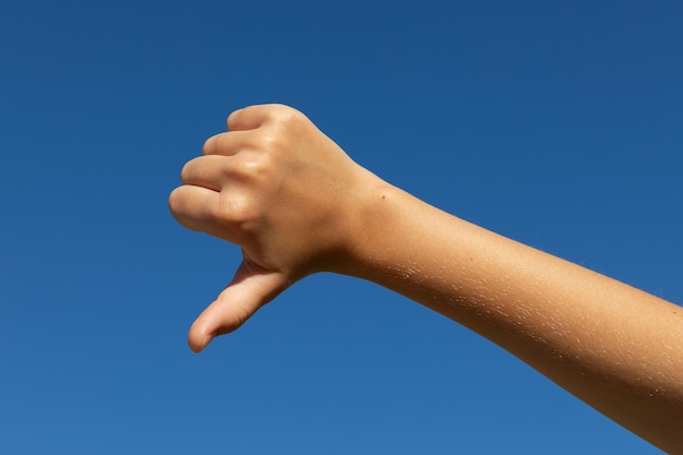 Child shows a thumb down gesture against a blue sky a concept on the topic of very hot sunny weather