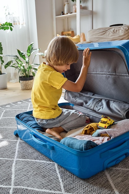 Child sitting in a suitcase and playing with a toy waiting for a trip to vacation