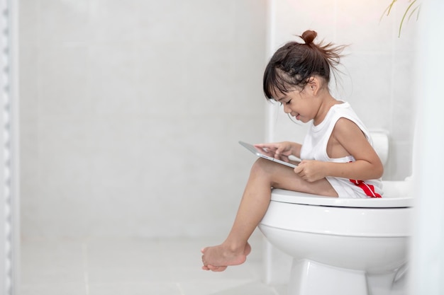 Child sitting on the toilet holding the tabletchild addicted smartphone concept