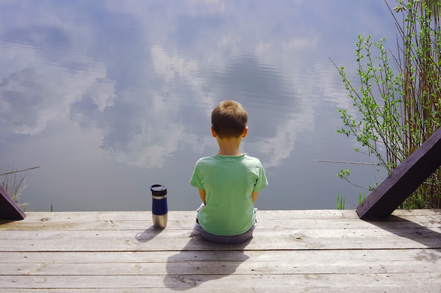 Child sitting on a wooden pier near the water. boy alone on the river.