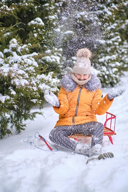 Child sledding sits on a sled and throws snow