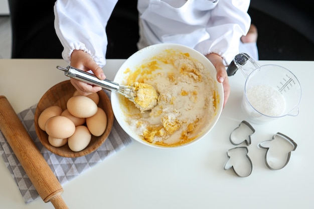 The child stirs the dough for shortbread cookies with a whisk