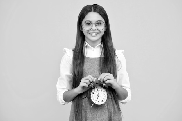 Child student girl with clock isolated on yellow background Child back to school Education and time concept Happy face positive and smiling emotions of teenager girl