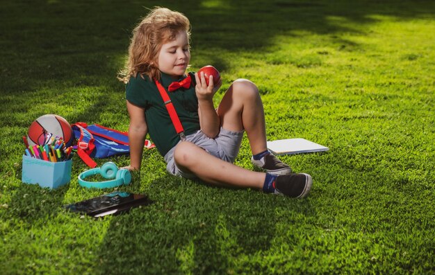 Child study in summer park cute little boy with school supplies sitting in elementary school park ea