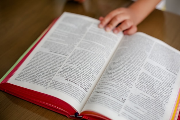 Child on the table reading the holy bible and leafing through it