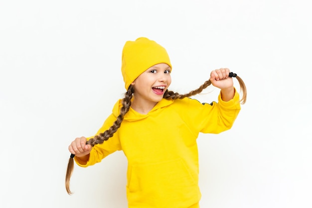 A child in a tracksuit and a yellow hat A beautiful little teenage girl with braids and a wide smile on a white isolated background