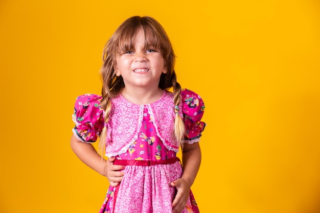 Child in typical clothes of famous Brazilian party called Festa Junina in celebration of Sao Joao Beautiful girl on yellow background