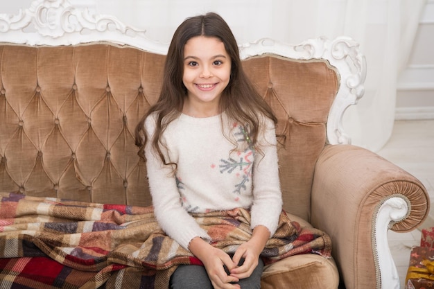 Child wear winter sweater enjoy holiday Happy new year Family winter holiday The morning before Xmas Santa please stop here Little girl relaxing on couch with blanket Cozy winter atmosphere