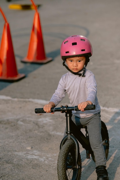 Photo a child wearing a helmet rides a bike with an orange cone behind him