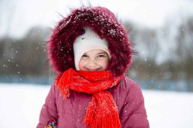 Child in winter A little girl in a warm hat and hood looks at the camera and smiles