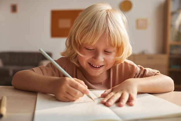 Child with blond hair writing the report in note book he doing homework after school