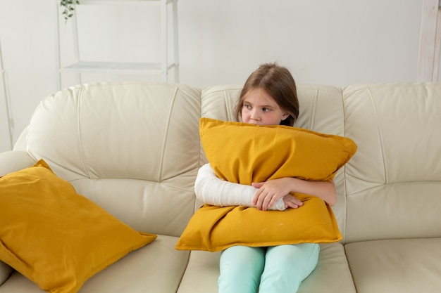 Child with a cast on a broken wrist or arm sitting on a couch