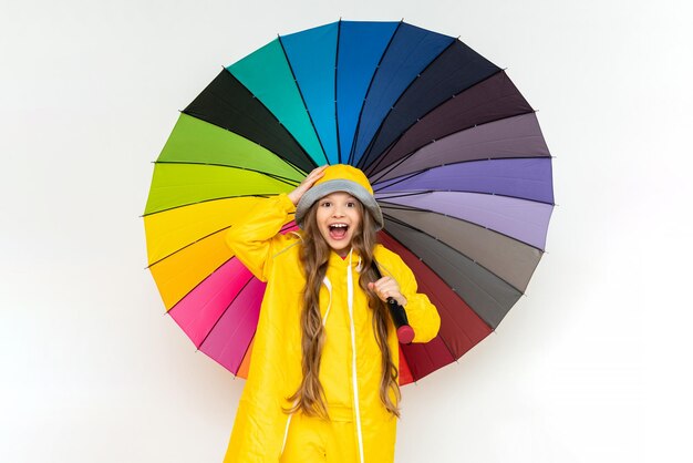 A child with a colorful umbrella in a yellow raincoat and a panama hat on a white isolated background