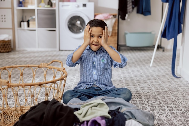 A child with dark hair sits on the laundry room floor in the bathroom a terrified boy clutching his head is doing housework tiredly sorting through a huge amount of clothes