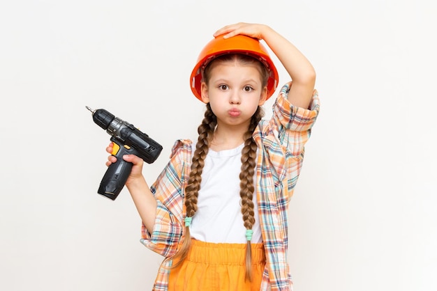 A child with a drill in his hands and wearing a protective construction helmetThe little girl wondered how to make repairs in the children's room The concept of repair