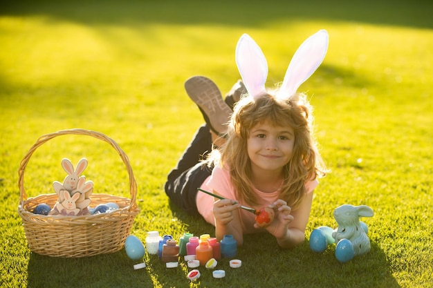 Child with easter eggs and bunny ears laying on grass painting eggs happy easter kids face