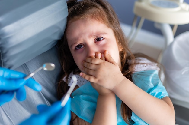 A child with her hands over mouth is looking at a dentist's tool