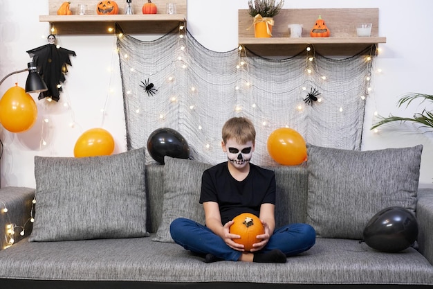 Child with makeup on his face paints a pumpkin for Halloween