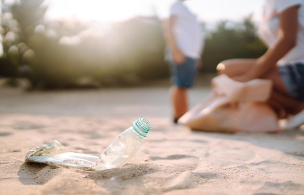 Photo child with mother collects plastic garbage on the beach by sea empty used dirty plastic bottles