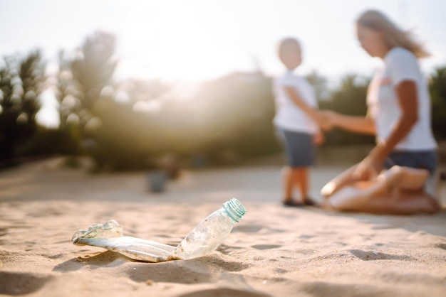 Photo child with mother collects plastic garbage on the beach by sea empty used dirty plastic bottles