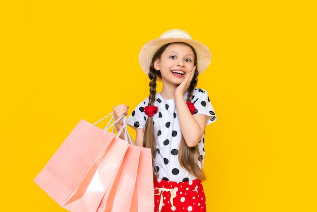 A child with paper bags from the store Summer shopping for children A beautiful little girl in a hat is smiling broadly Yellow isolated background