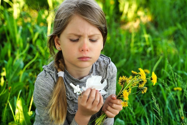 Child with pollen allergy Girl sneezing and blowing nose because of seasonal allergy Spring allergy concept Flowering bushes and trees in background Child allergy