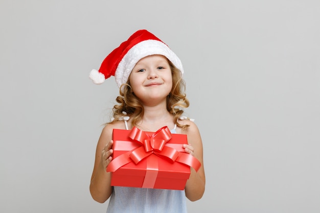 A child with a Santa hat is holding a red gift box