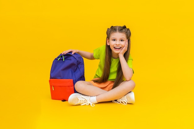 A child with a school backpack Educational courses for junior and secondary schools A charming little girl is going to school on a yellow isolated background