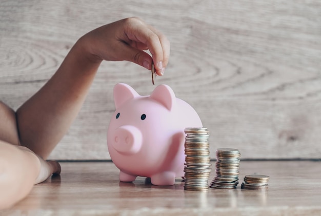 Child woman hand putting money coin into piggy bank for saving money for education study or investment Stack coins Save money concept