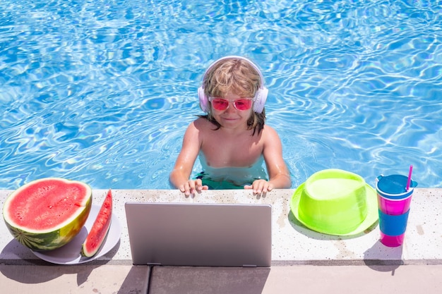 Child work outside with laptop in pool Kid working on laptop from the swimming pool Summer business