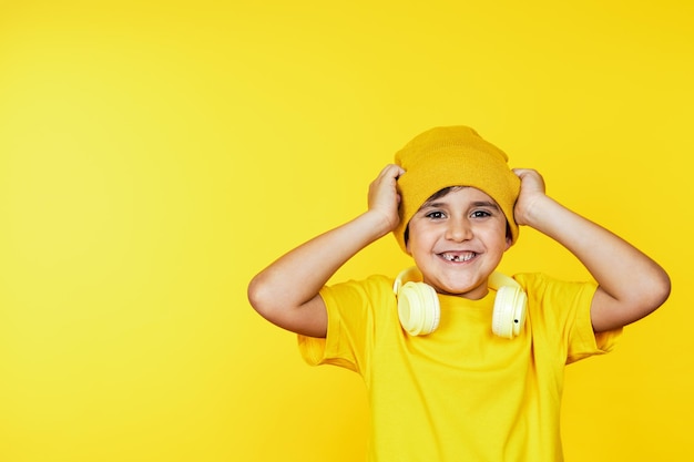 Child in yellow attire adjusting beanie white headphones around neck against a bright backdrop