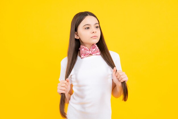 Childhood concept Portrait of smiling teenage girl in tshirt with bowtie isolated on yellow background