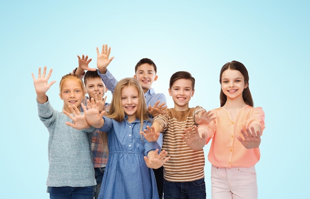 childhood, fashion, friendship, gesture and people concept - happy smiling children waving hands over blue background