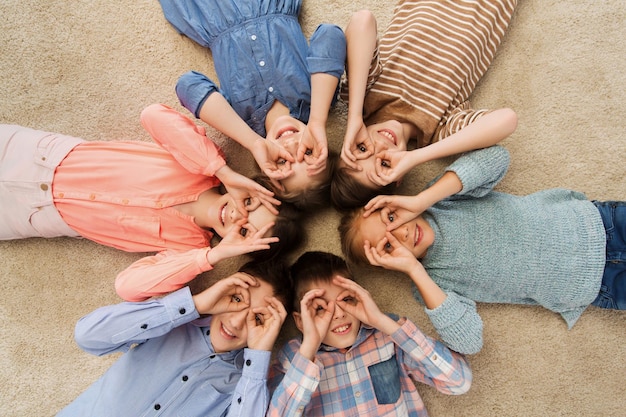 childhood, fashion, friendship and people concept - happy children lying in circle on floor, making faces and having fun